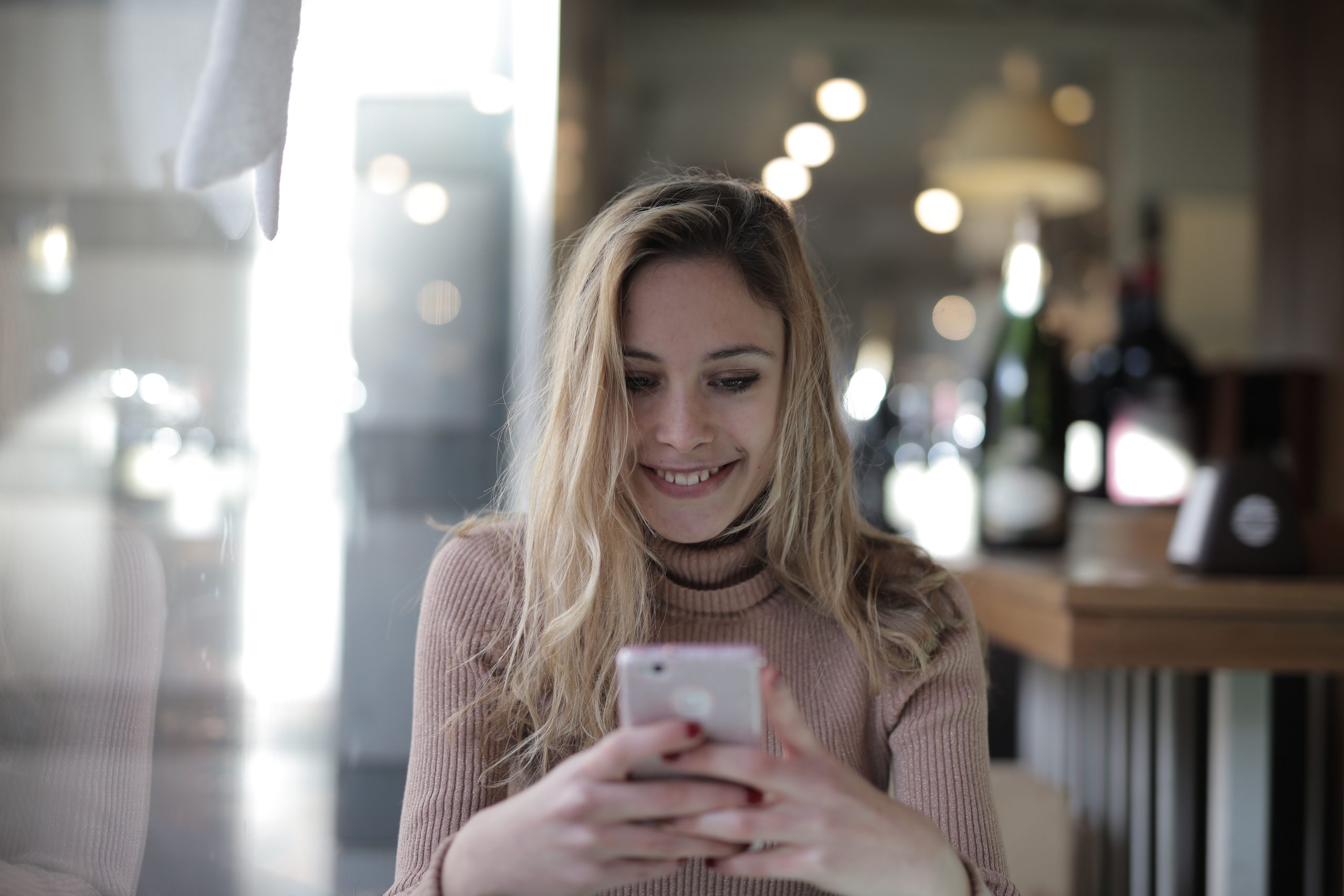 Happy customer smiling while using her smartphone at a cafe, about to leave a review